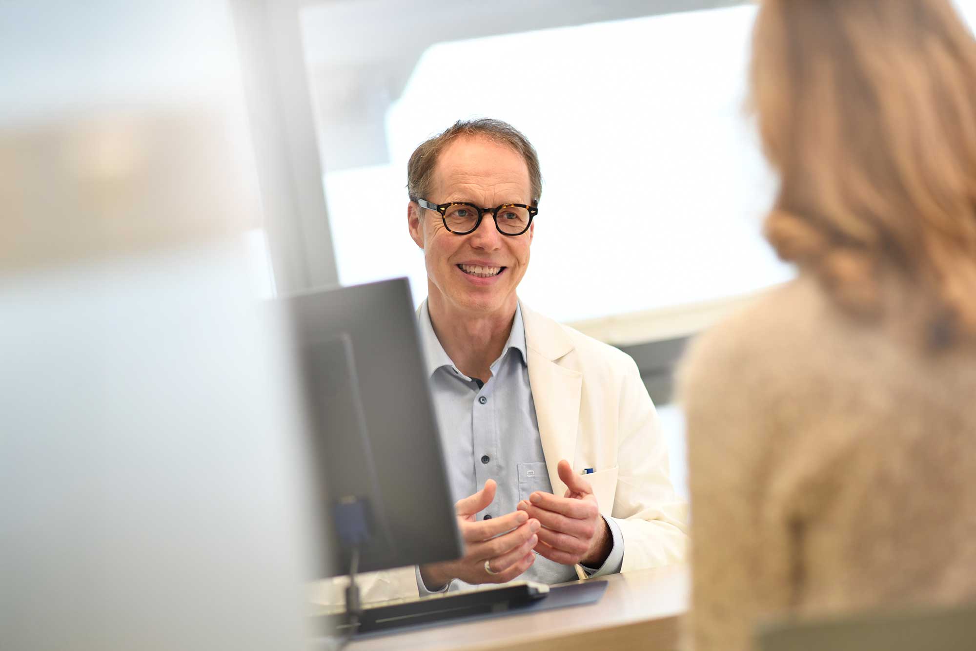 Arzt im Gespräch mit Patientin am Schreibtisch