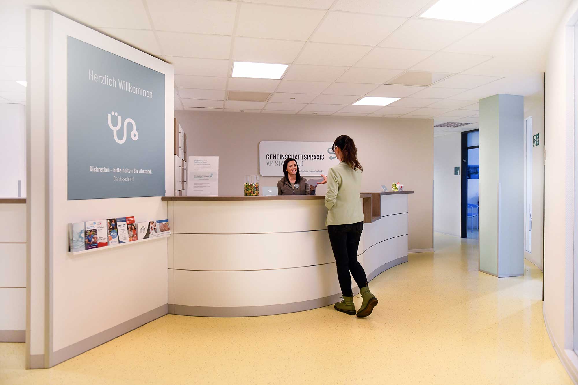 Empfangsbereich der Gemeinschaftspraxis, Praxismanagerin reicht Dokumente an Patient